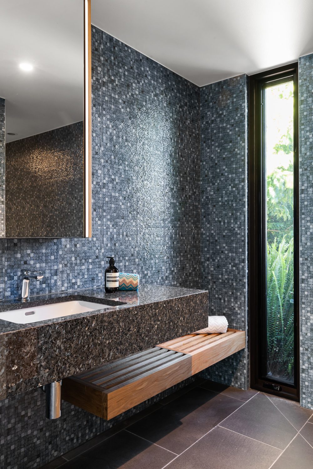 Mosaic-tiled bathroom with stone vanity and timber shelf, inner-east new build